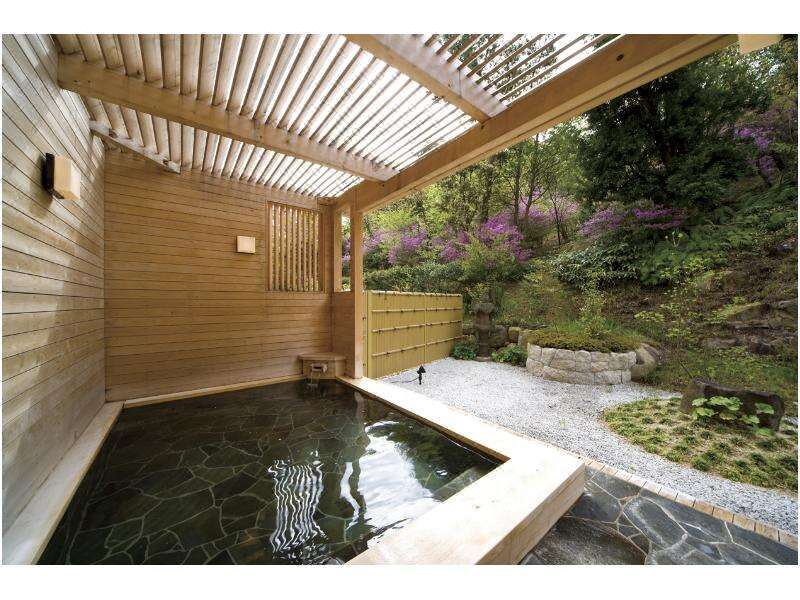 Private stone-lined open-air bath beneath a timber canopy beside a garden.
