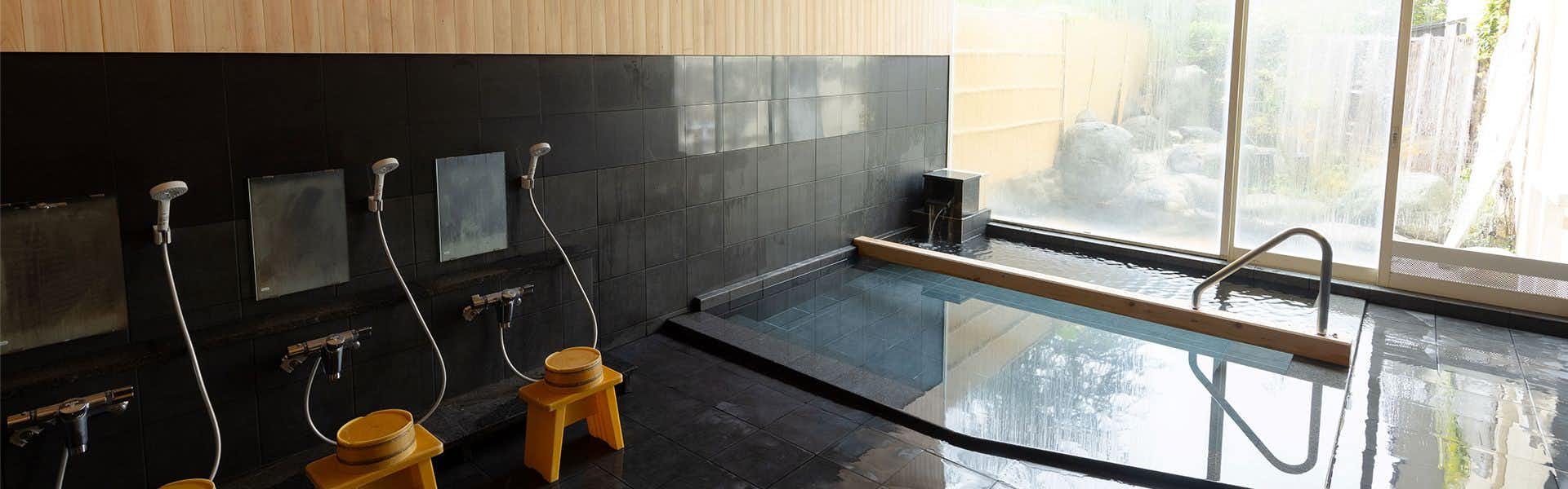 Onogawa Onsen Takasagoya with an indoor bathing area with wall showers and a long soaking tub.
