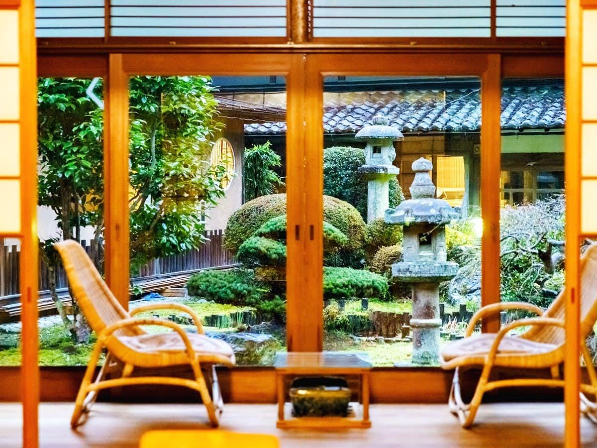 Guest Villa Aisakura with two wicker chairs overlooking a stone lantern and green garden.