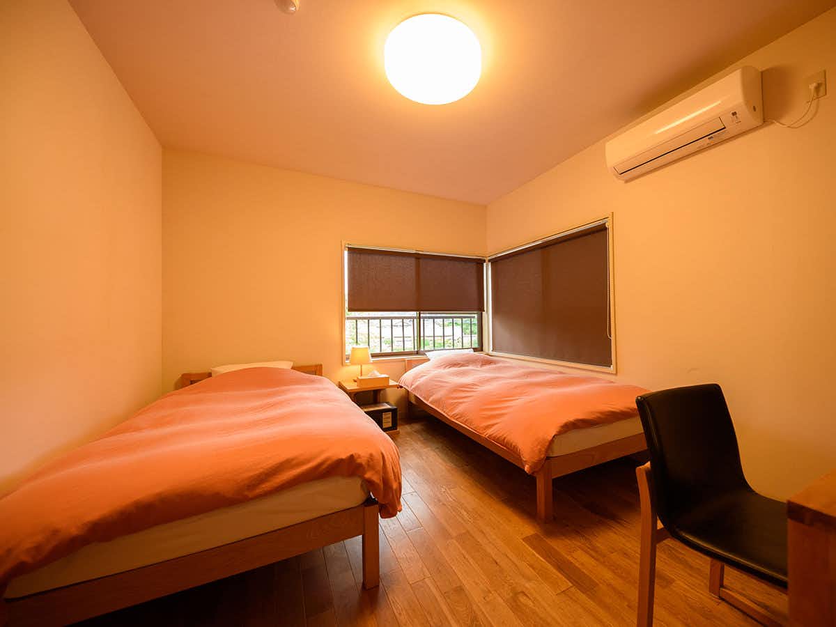Yufuin Iyotomi with a simple twin bedroom with coral bedding and timber floor.
