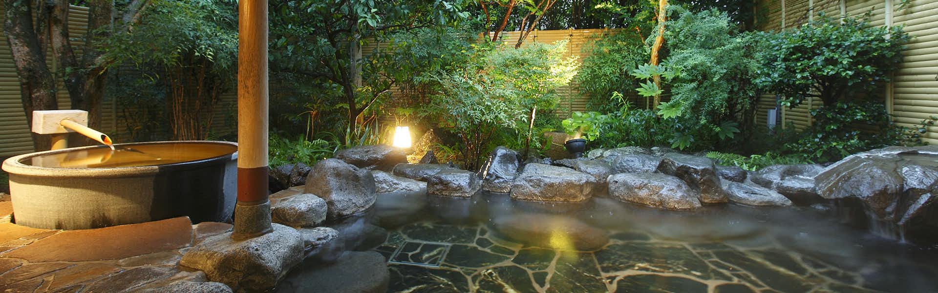 Yumeguri no Yado Yoshiharu outdoor bathing area with large boulders, flowing water stream, and dense forest vegetation surrounding wooden structures