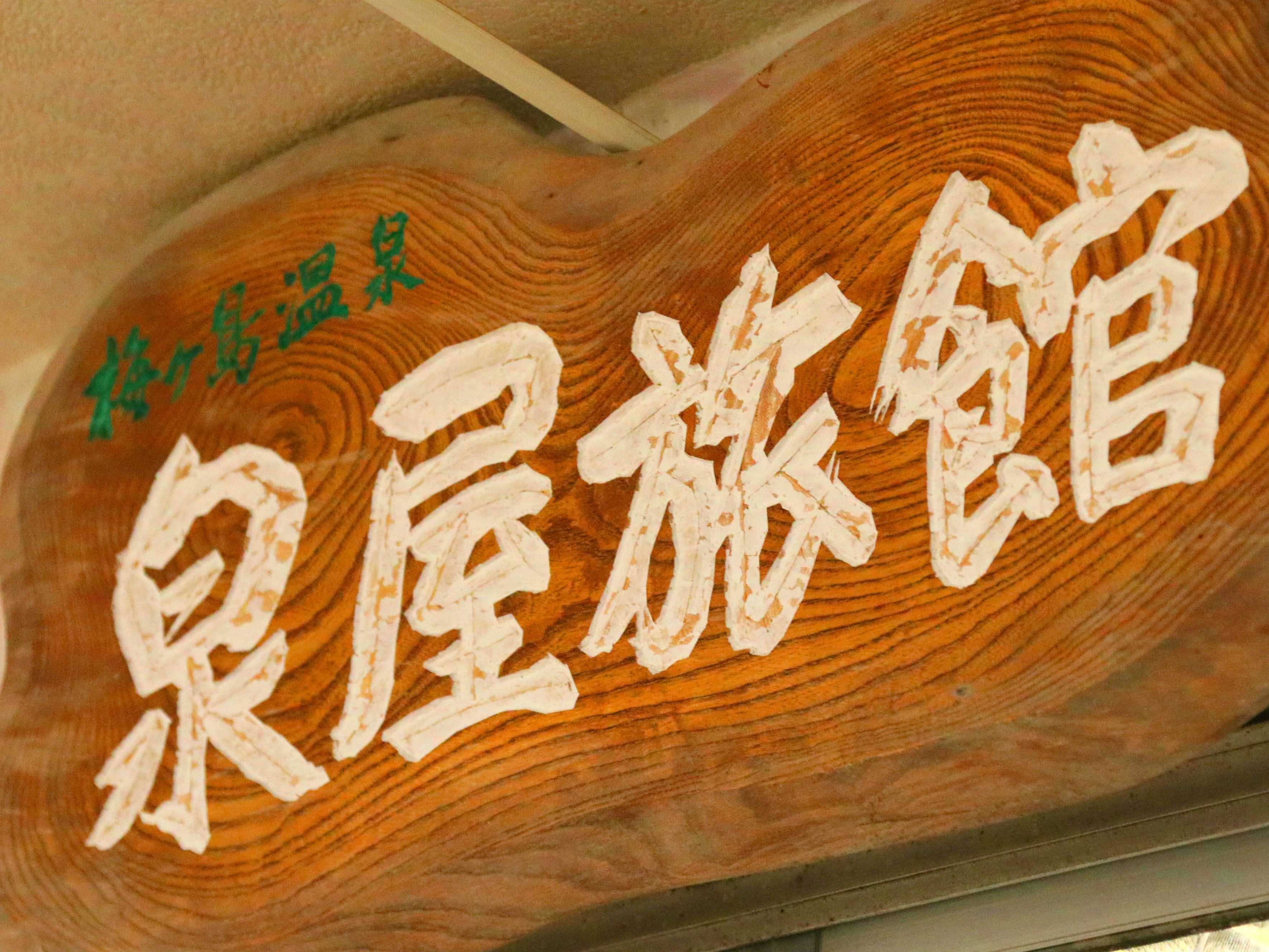 Umegashima Onsen Izumiya Ryokan with the carved timber property sign beneath clear blue sky.