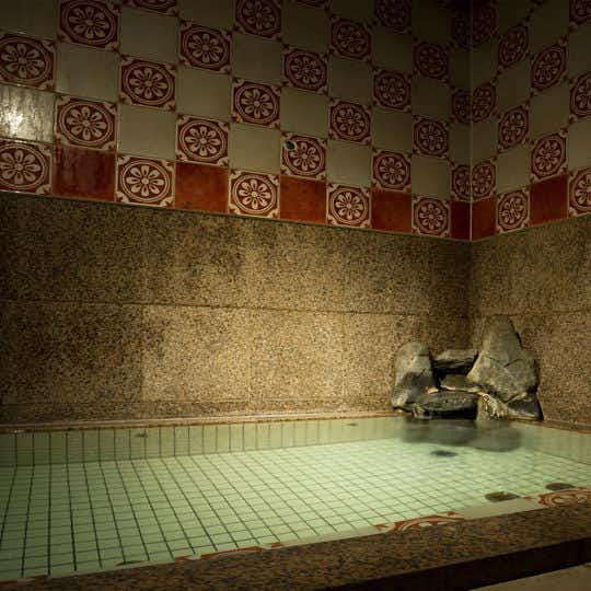 Hanakoji Saigetsu Rectangular tiled bath beneath patterned wall tiles with a rock water spout and subdued lighting