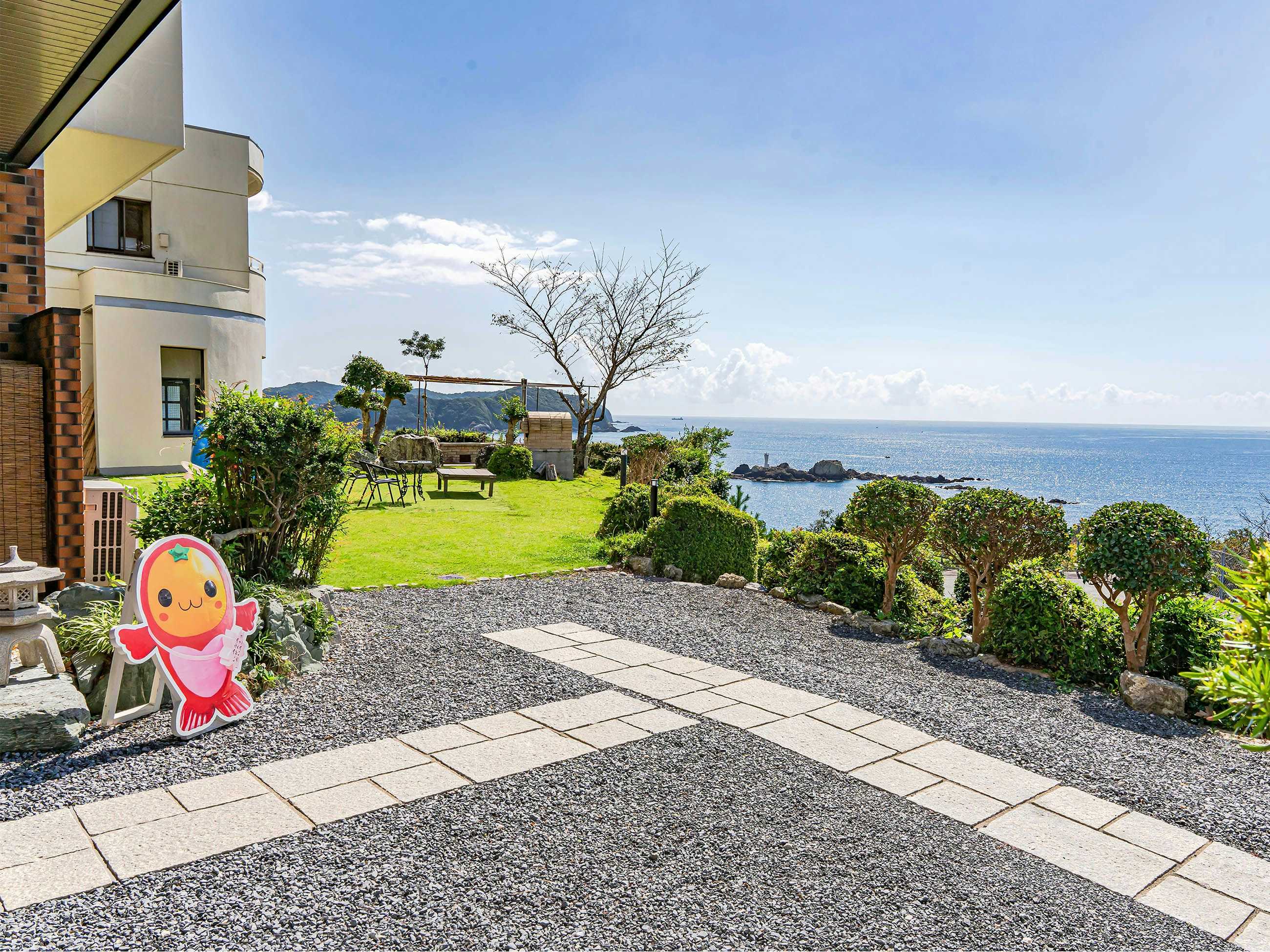 New Hamaguchiya Ryokan with the landscaped seaside forecourt beside a colorful welcome figure.