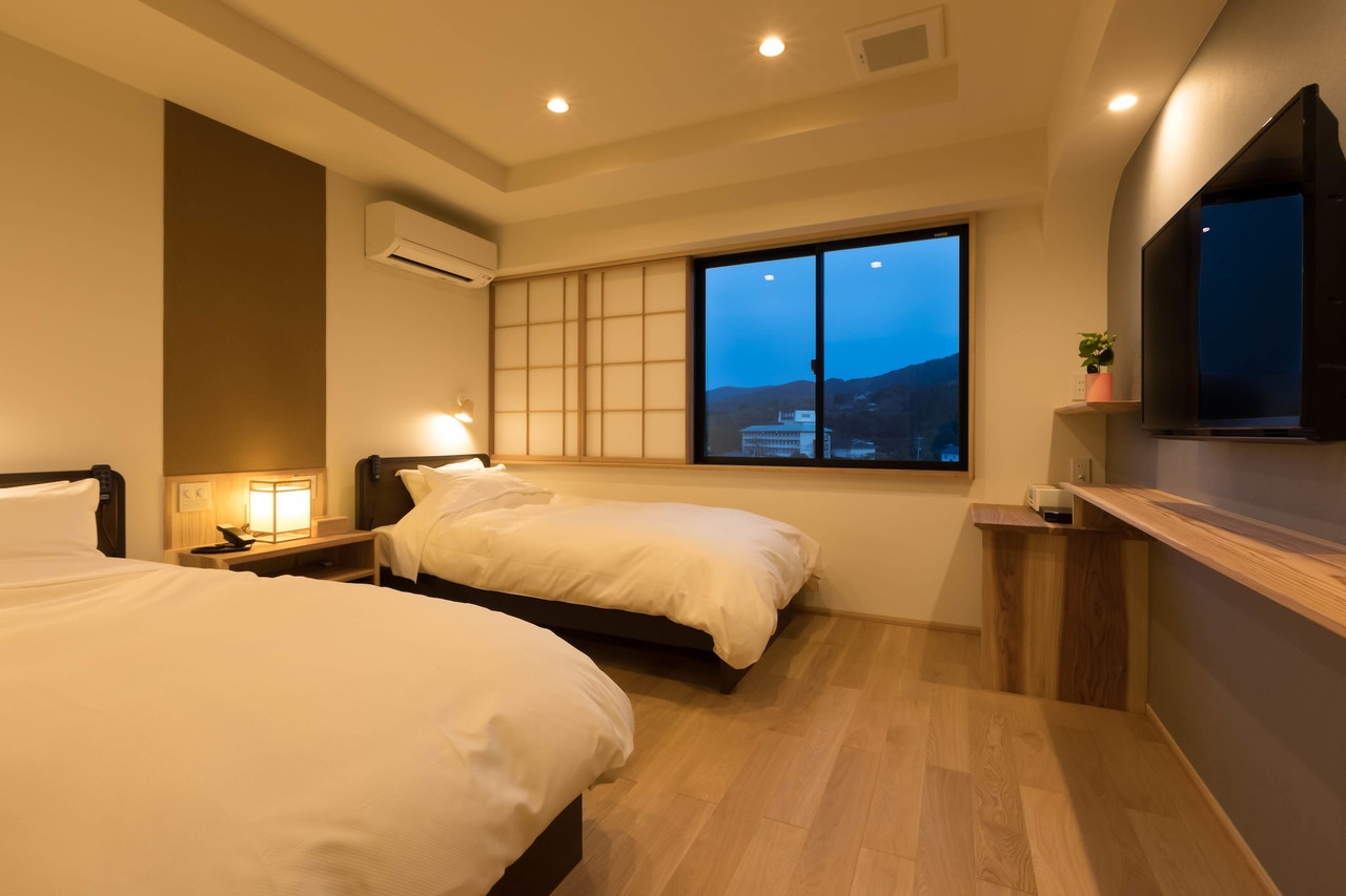 Guest room with twin beds, a desk, and a wide window.