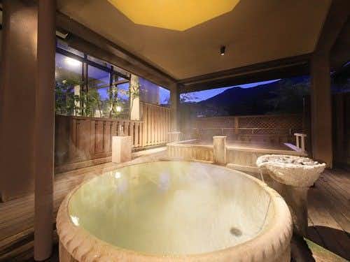 Yugawara Ohnoya Ryokan with a round private soaking tub beside windows overlooking a wooded terrace.