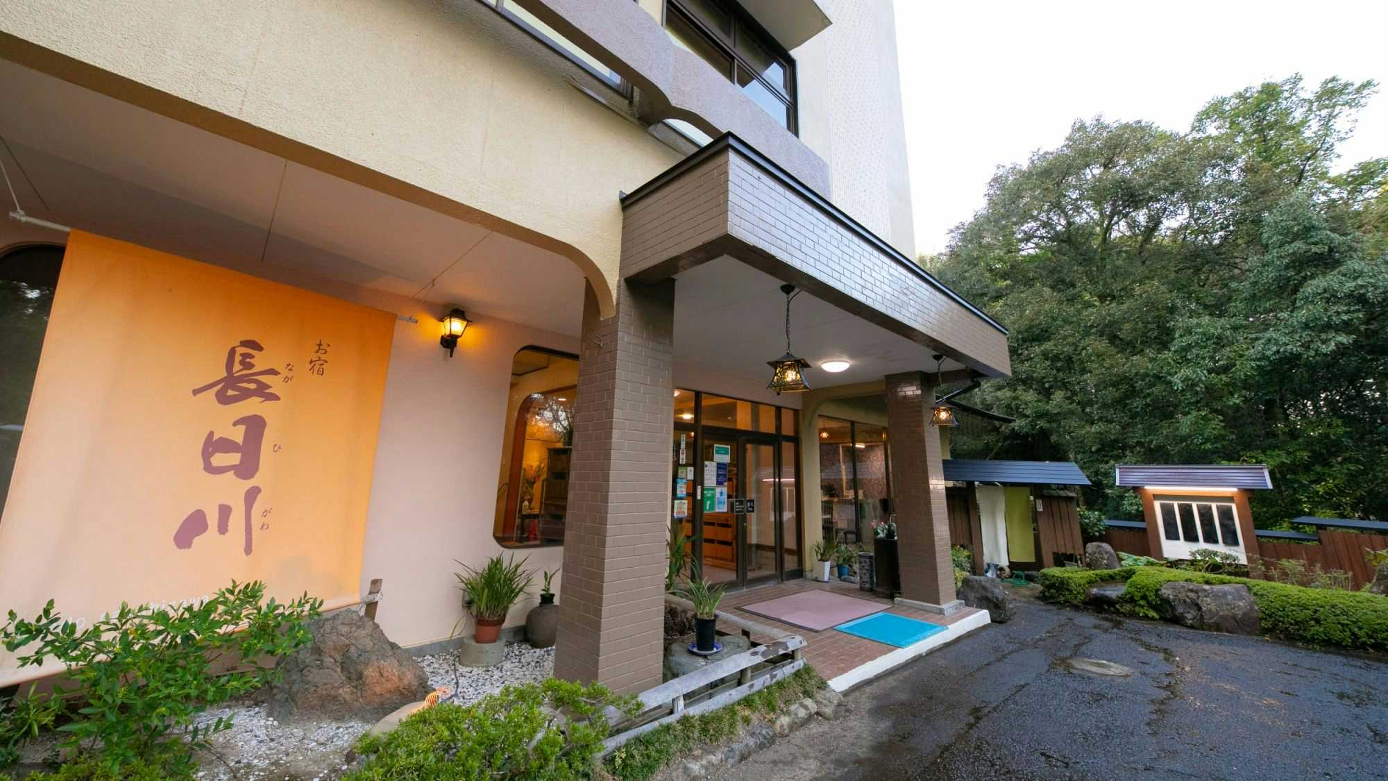 Nagahikawa: An Irori Kaiseki Inn in the Hidden Retreat of Miyazaki with a modest entrance surrounded by trees and shrubs.