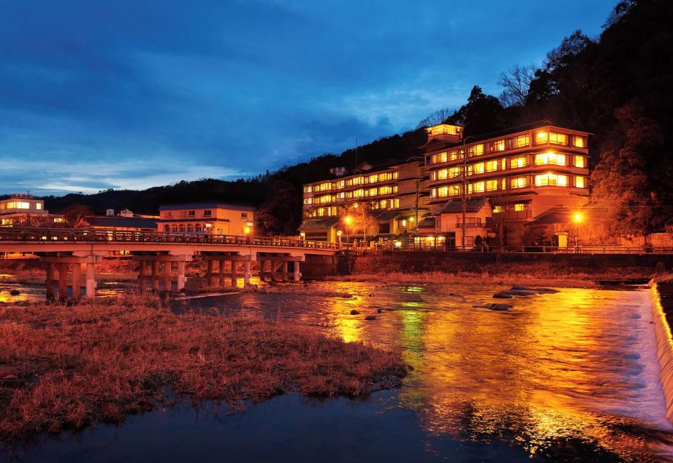 The ryokan buildings illuminated beside the river at night.