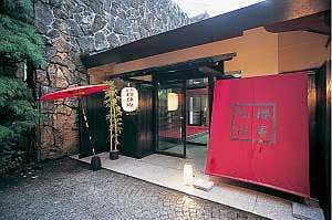 Sakura Kyuan: An Inn with Natural Hot Spring Flow Traditional gate with red walls, dark timber doors, paper lantern, red parasol, stone wall, and gravel path