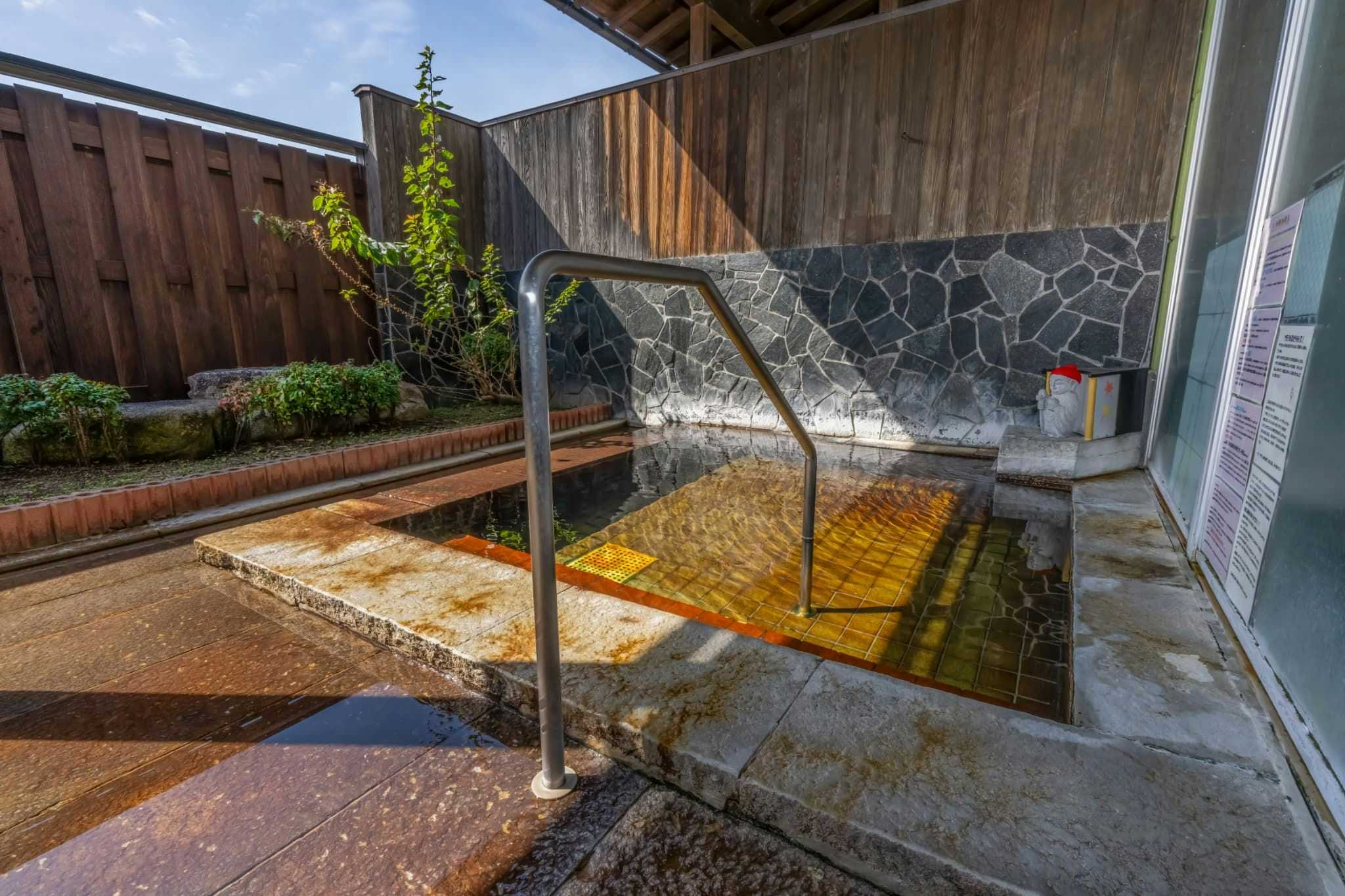 Harazuru Onsen Enmeikan with an outdoor mineral bath beside timber walls and garden planters.