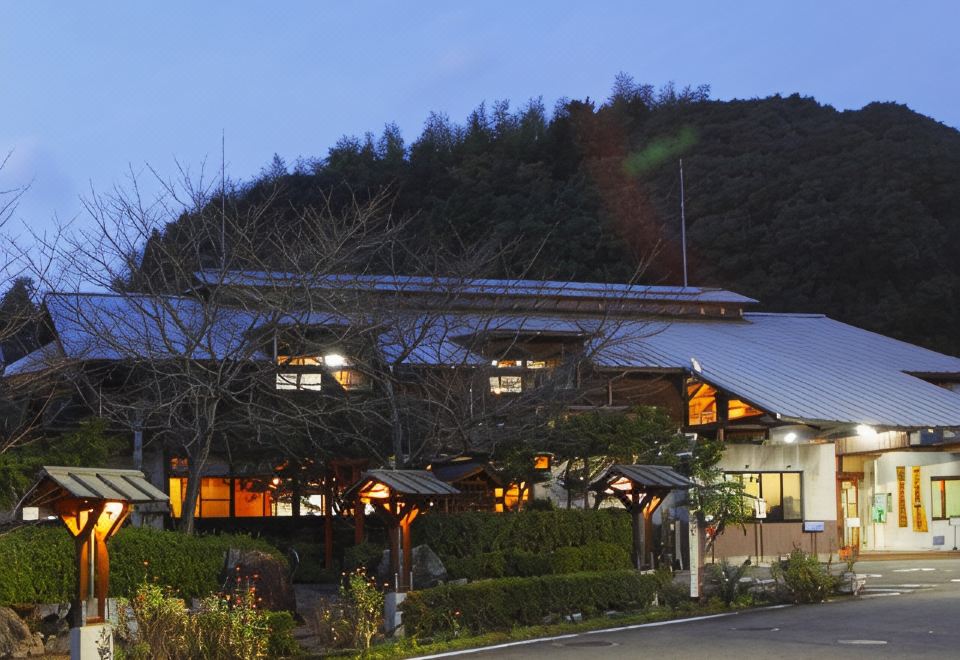 A traditional inn glows beside a wooded hillside.