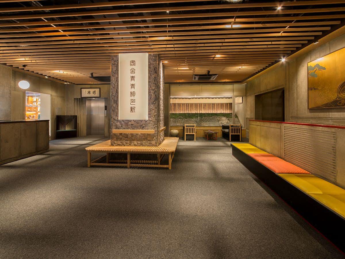 Ryokan Kouro with a quiet lobby with central bench and property name pillar.