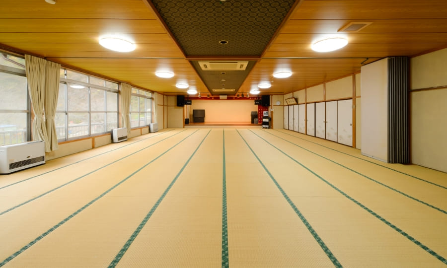 An empty, spacious tatami banquet hall beneath a coffered ceiling.