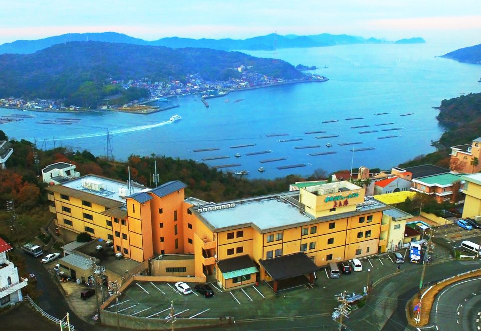 A large hotel building overlooks a blue bay dotted with floating aquaculture platforms.