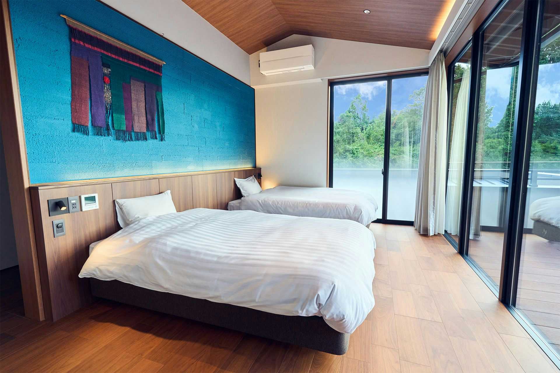 Hitoyoshi Onsen Ishinono-yu Ichifuji Ryokan with a bright twin bedroom, turquoise accent wall, and garden doors.