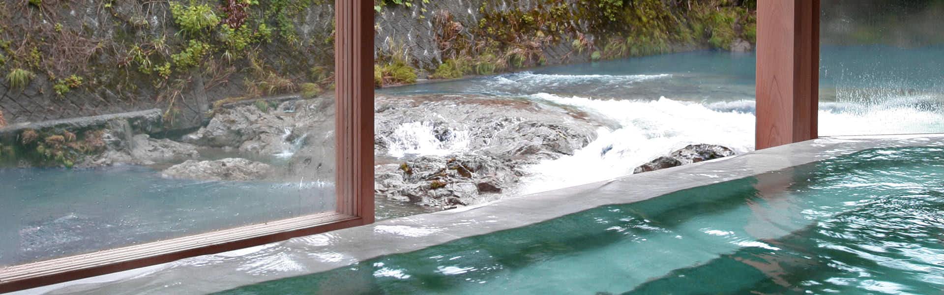 Tomoya Hotel with a turquoise indoor bath overlooking a rocky mountain river.