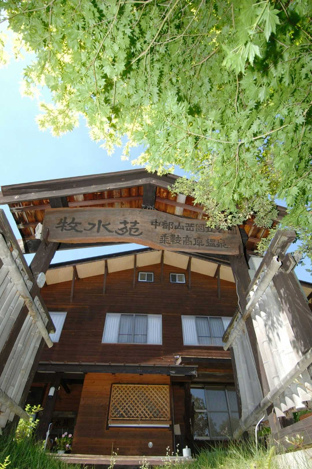 Bokusui-en timber lodging exterior framed by an entrance gate and leafy tree