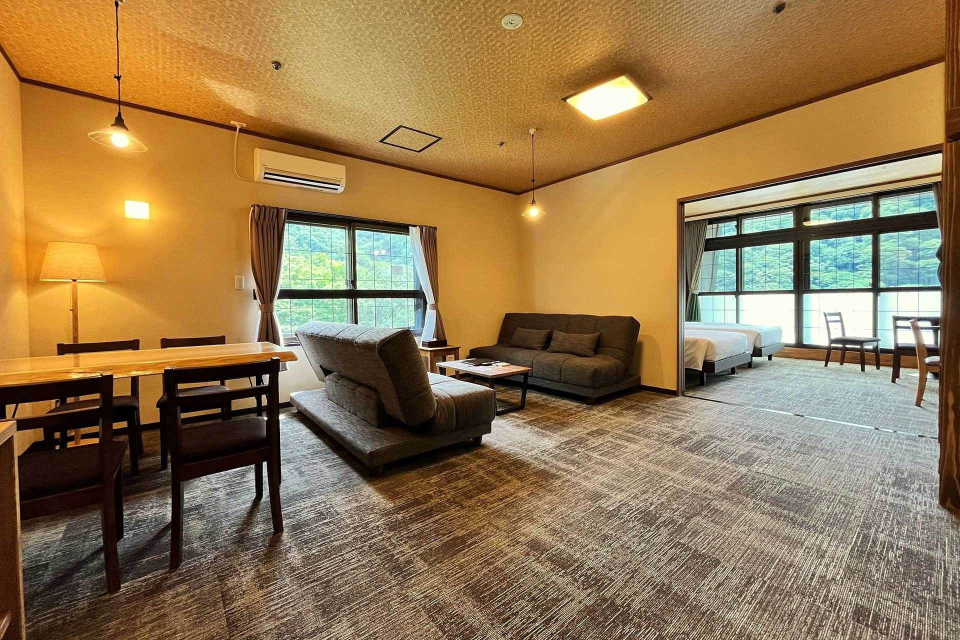 Kutsurogijuku Shintaki Spacious room with dining table, sofas, armchairs, large windows, and a separate sleeping area beyond