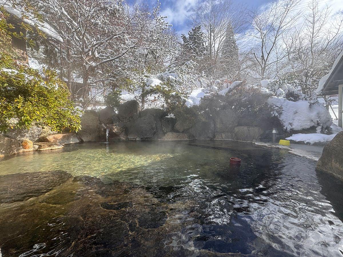 Tsudoi-yu and Soba Cuisine Inn Seigakukan with an outdoor rock bath surrounded by snowy trees.