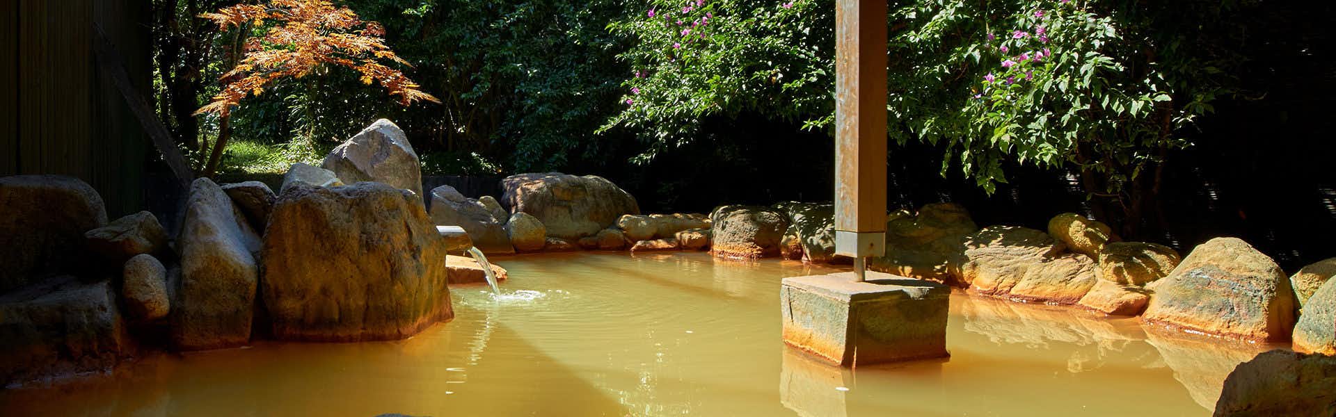 Koran no Yu Kinkouro Bath or pool with golden-toned water, stone edges, and wooden structural elements visible overhead.