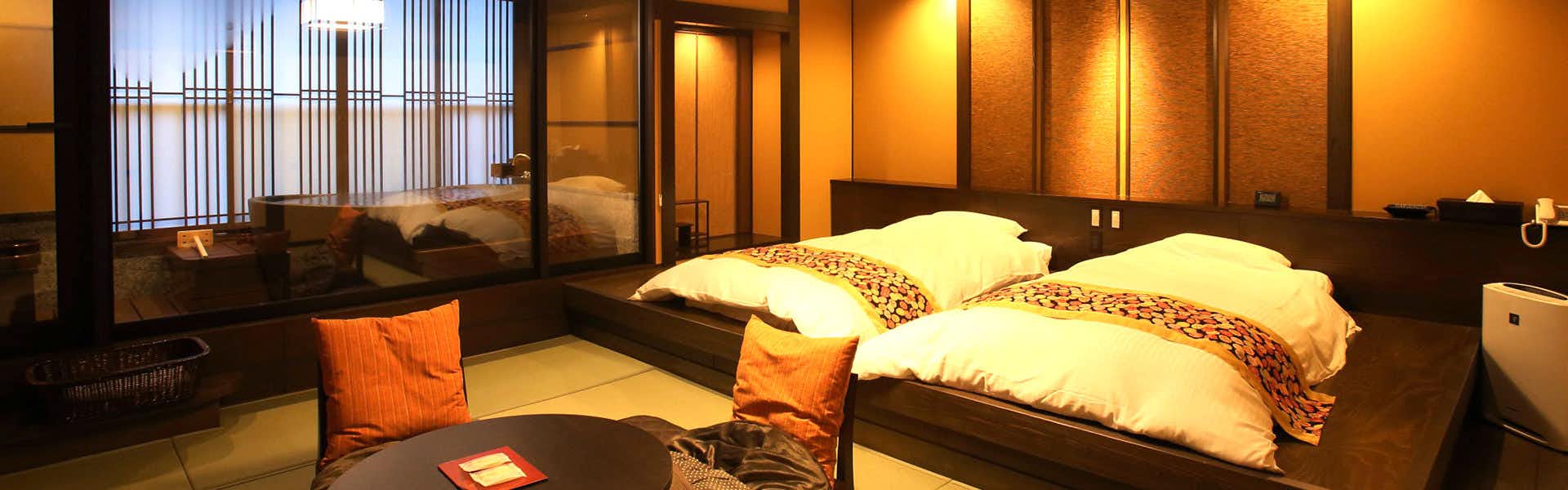 Fukumitsu Hanayama Onsen twin-bed room with floor seating and a glass-walled bath beyond