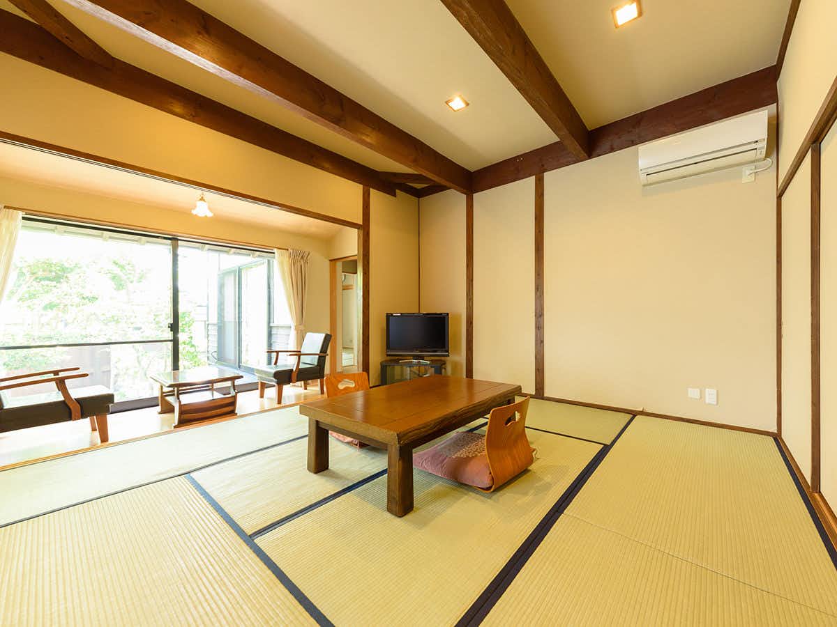 Yufuin Onsen Tsukanoma with a bright tatami room with a low table, chairs, and mountain-facing windows.
