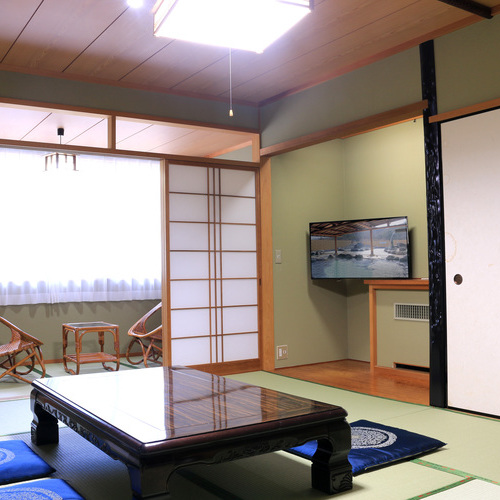 A tatami guest room with a low table, television, and window-side chairs.