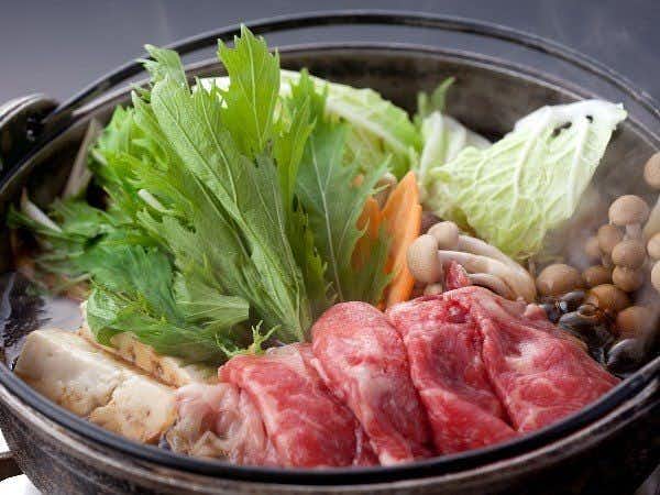 Shoen dark pot filled with prepared items and leafy greens