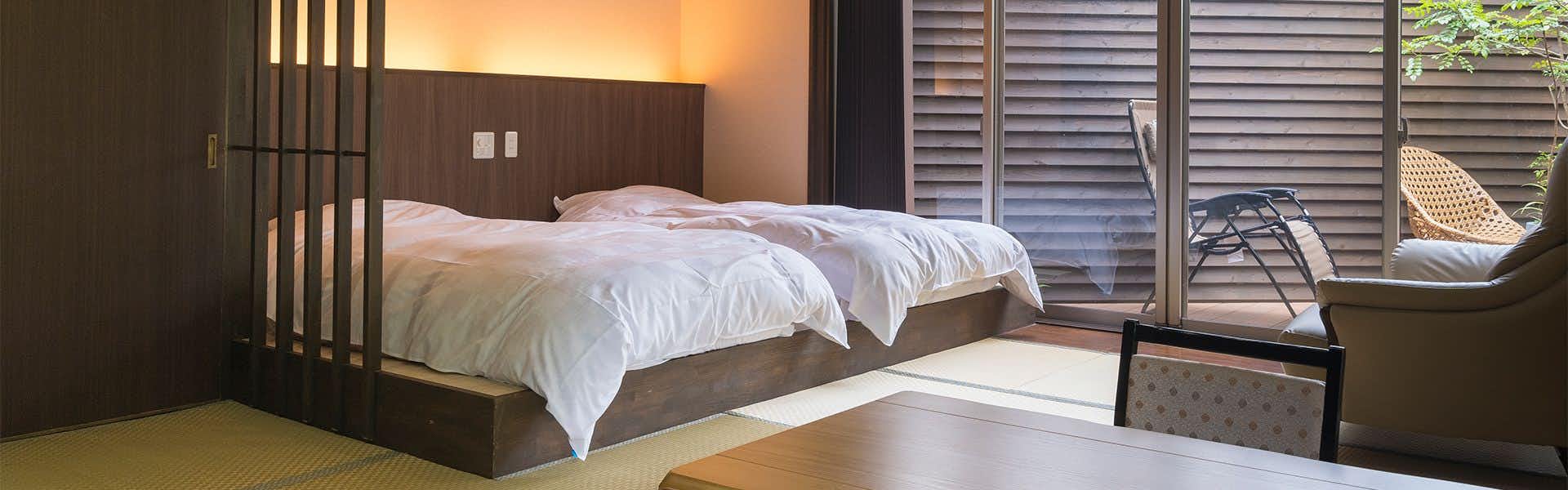 Ureshino Oyado Kujyaku: A modern bedroom opening toward a private timber terrace.