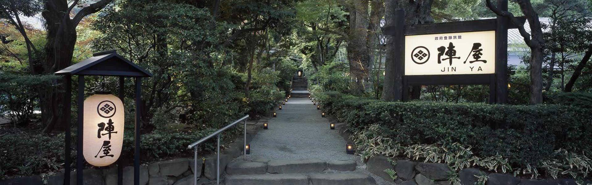 Motoyu Jinya Entrance pathway with stone walkway, lantern sign, traditional buildings, and landscaped garden with mature trees