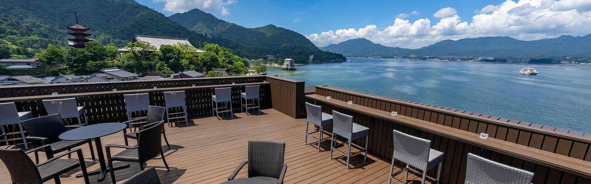 Miyajima Kinsuikan a rooftop terrace with tables facing the bay and mountains.