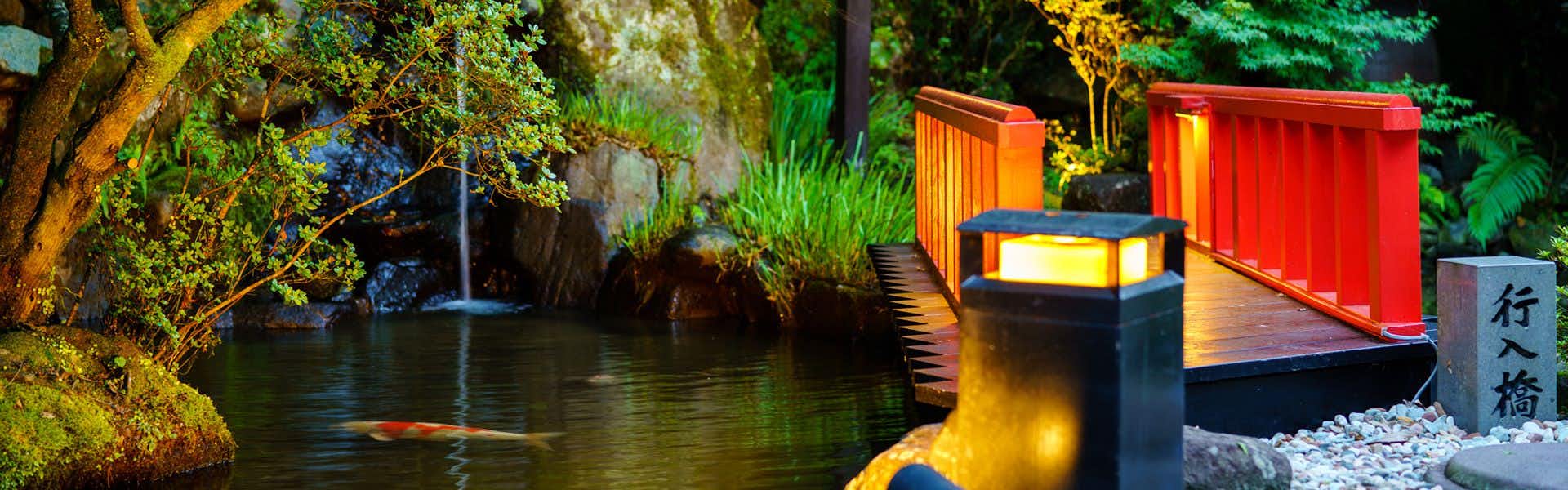 Beppu Showa-en with a red bridge reflected in a shaded garden pond.