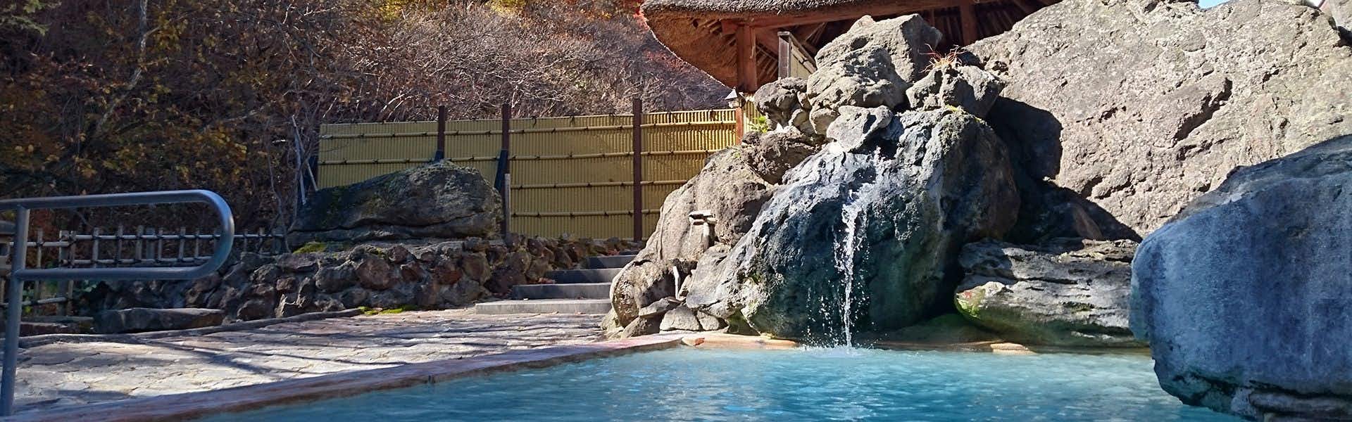 Ryokan Tamagoyu with an open-air stone bath beneath natural rock walls.