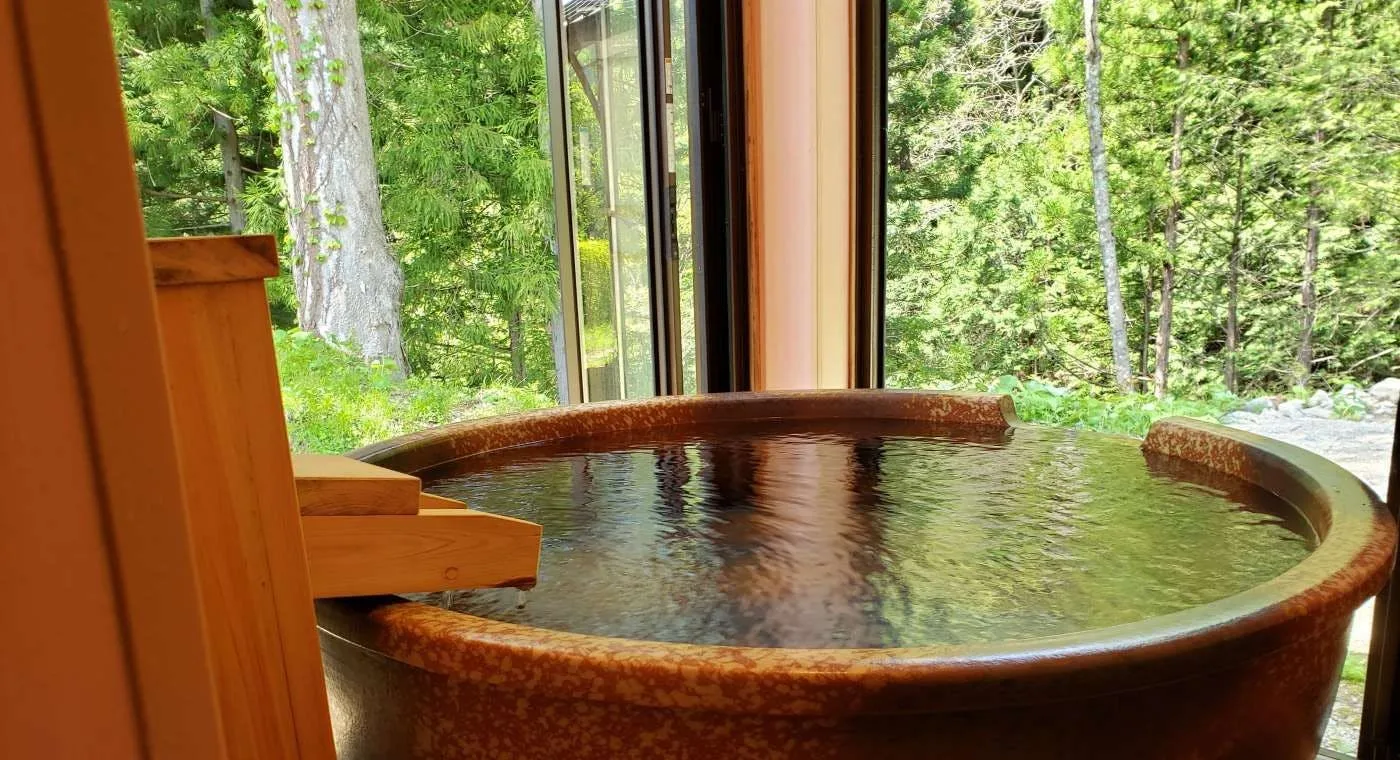 Round ceramic in-room bath overlooking dense cedar forest at Yunishigawa Onsen