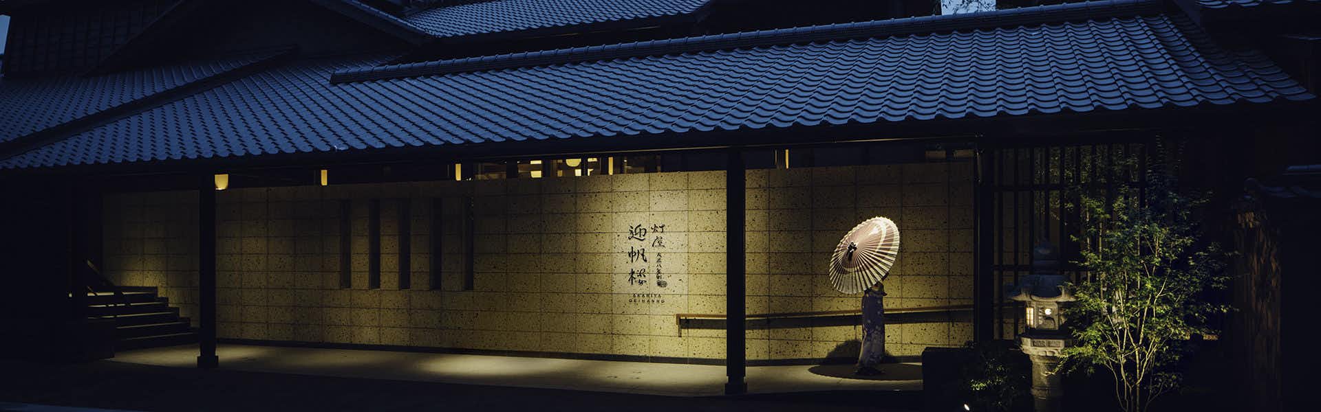 Akariya Geihanro Traditional Japanese building entrance illuminated at night with blue-tiled roof and landscaping visible.