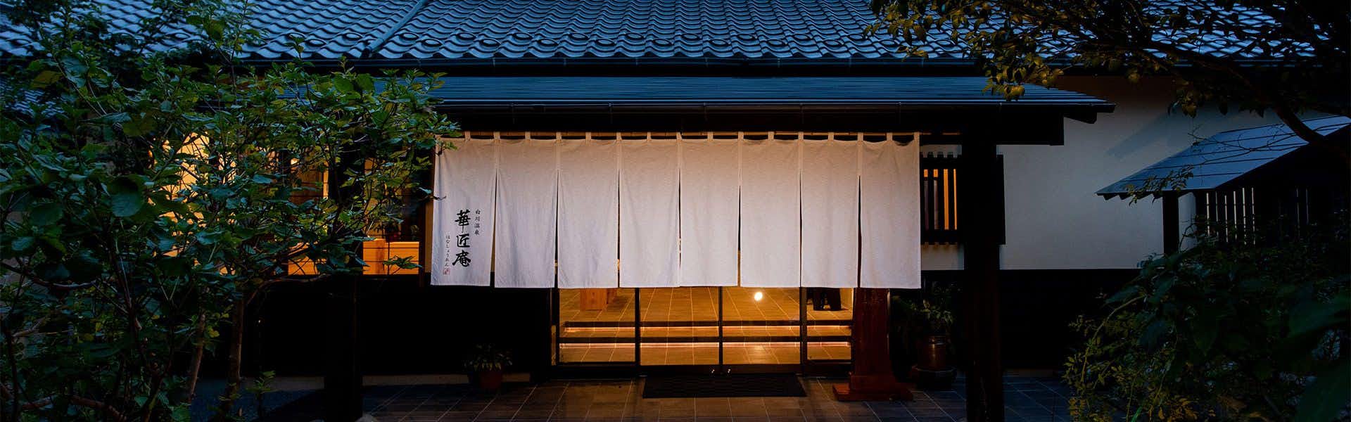 Shirakawa Onsen Kashoan an entrance facade with a white noren curtain beneath trees.