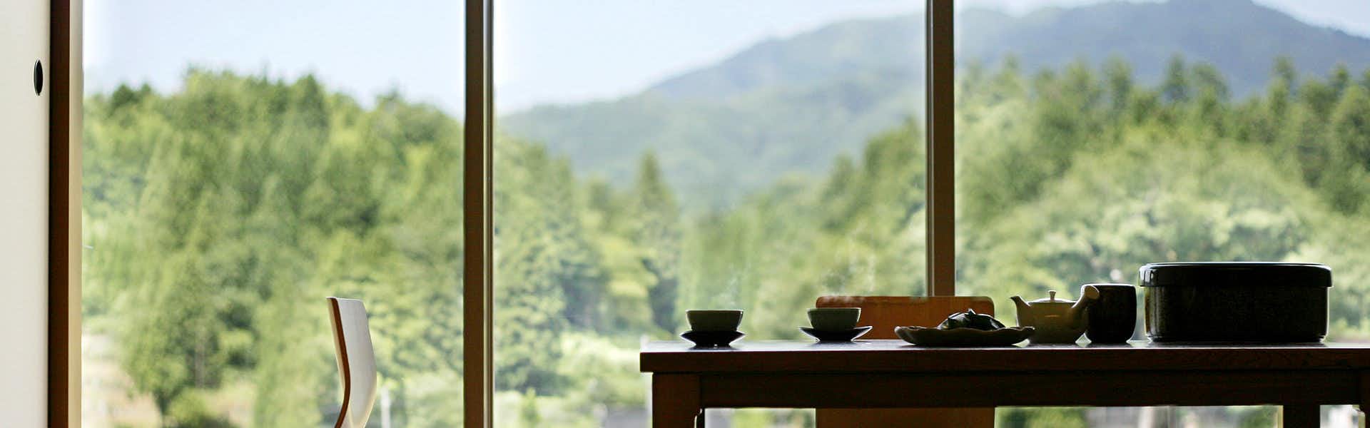 Kamedake Onsen Tamamine Sanso with a breakfast tray beside windows framing green mountains.
