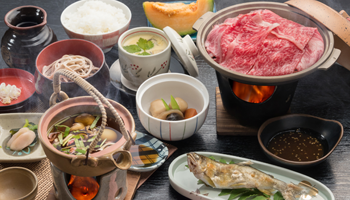A spread of dishes includes sliced meat, rice, soup, and small side plates.