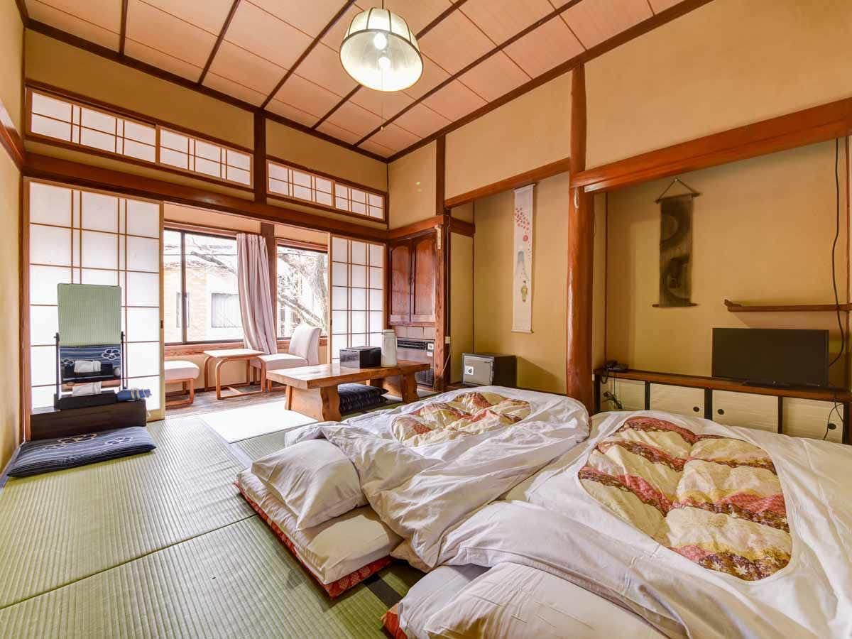 A sunlit tatami room prepared with patterned futon bedding.