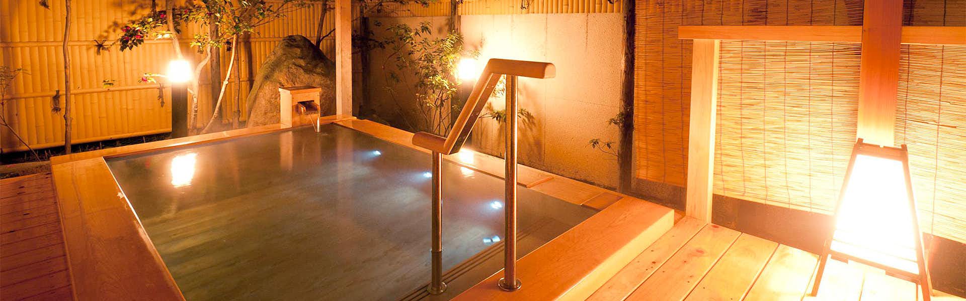 Shinshu Togura Kamiyamada Onsen Kihinkan Ryotei Takano Square wooden bath beneath warm lights with bamboo blinds, timber decking, metal handrails, and a garden wall