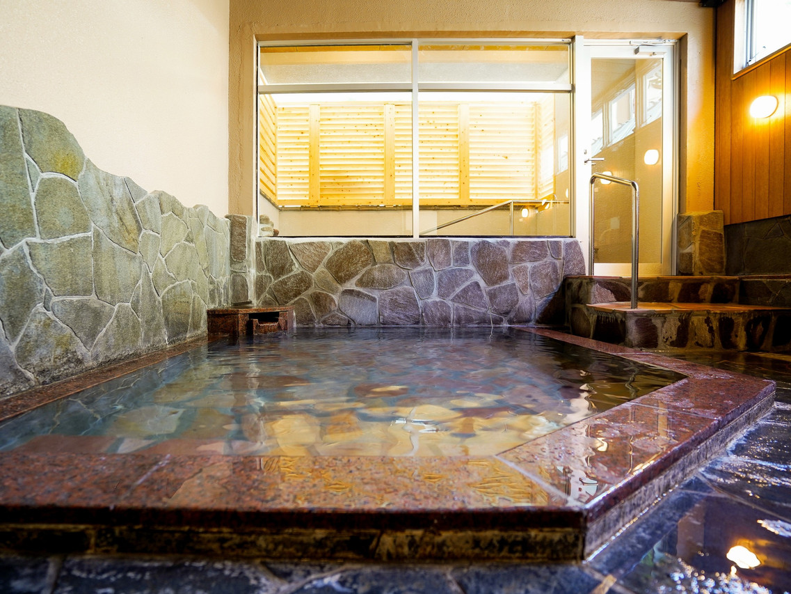 A stone-lined indoor bath with large windows.