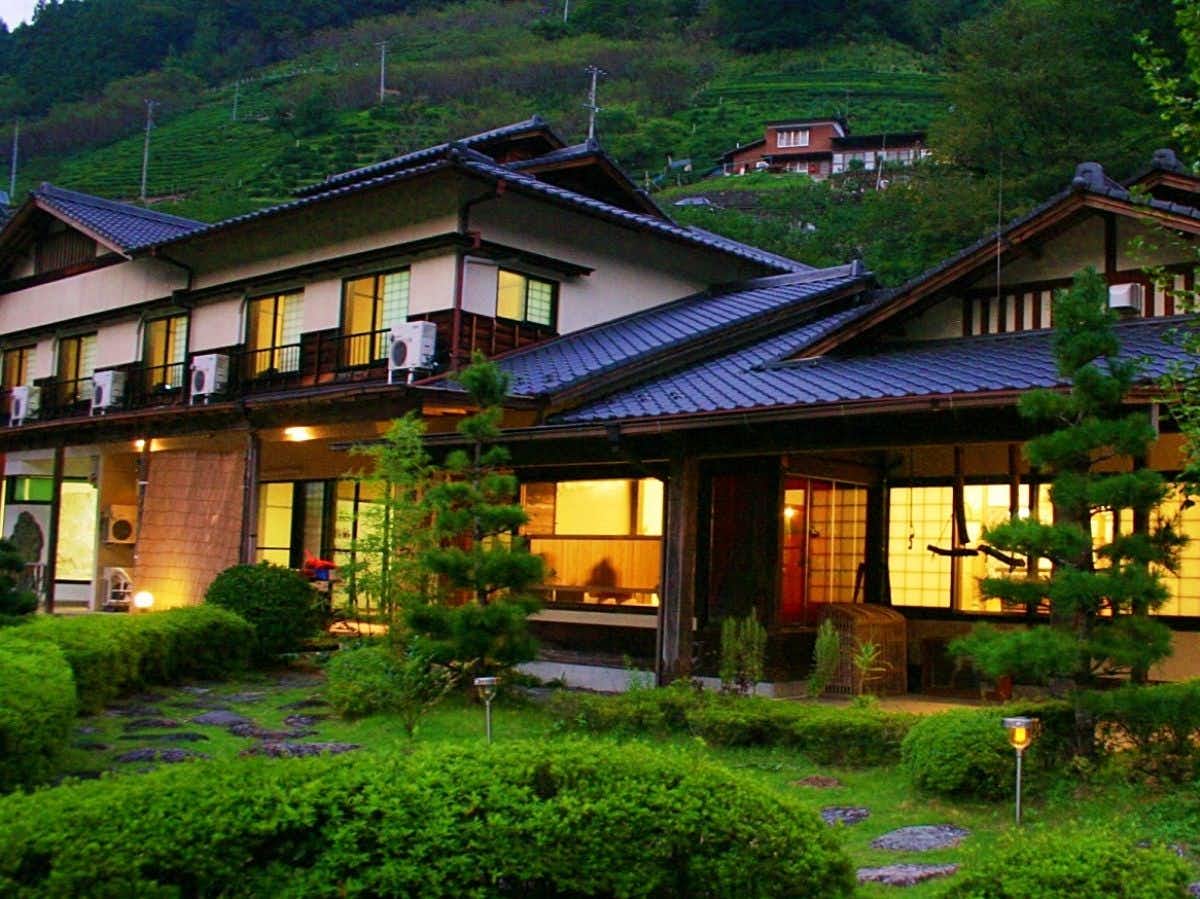 Irori no Yado Shimabatake with this scene, where shimabatake's timber buildings and clipped garden stand beneath forested hills.