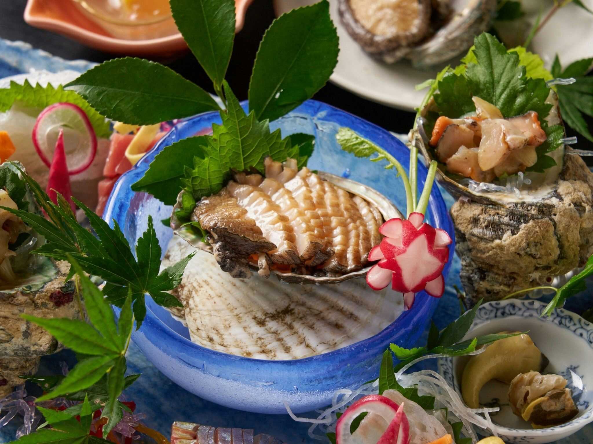 Ohamaso Prepared portions in a blue bowl with green leaves and carved red garnish, surrounded by patterned dishes