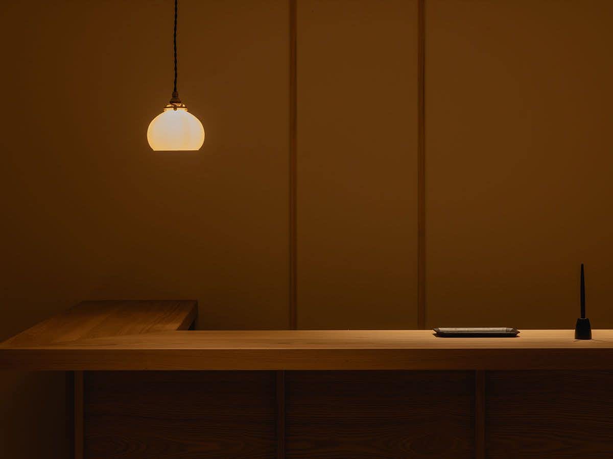 A pale timber reception desk beneath a pendant lamp.