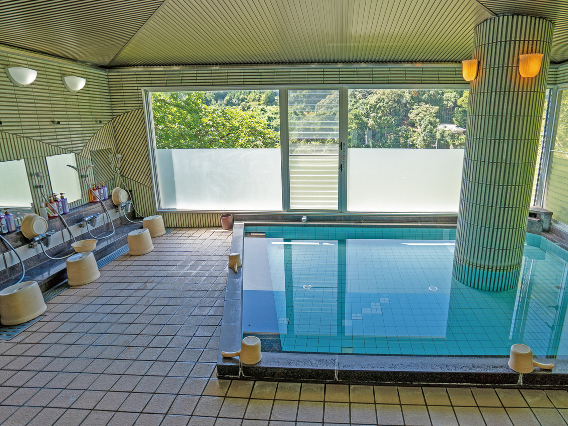 An indoor bath beside a row of washing stations and large windows.