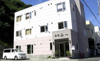 A white three-story lodging building with a car parked beside the entrance.