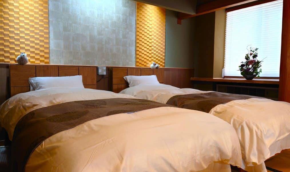 Kusatsu Onsen Yuyado Iwafuji with twin beds, patterned wall panels, wood trim, and a flower vase