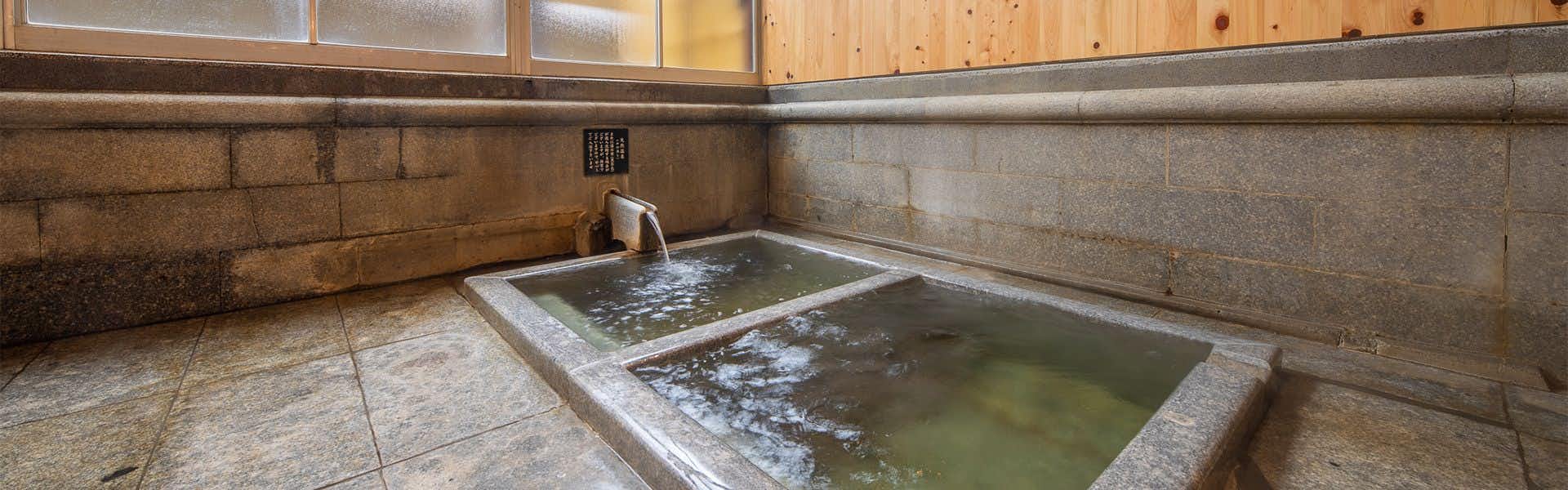 Hitoyoshi Onsen Ryokan Suiranro with a square stone tub, pale tile walls, and wood window panels