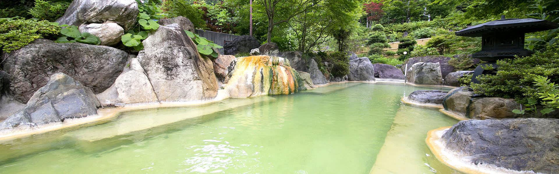 Okuhida Garden Hotel Yakedake with an outdoor mineral bath surrounded by rocks and garden greenery.