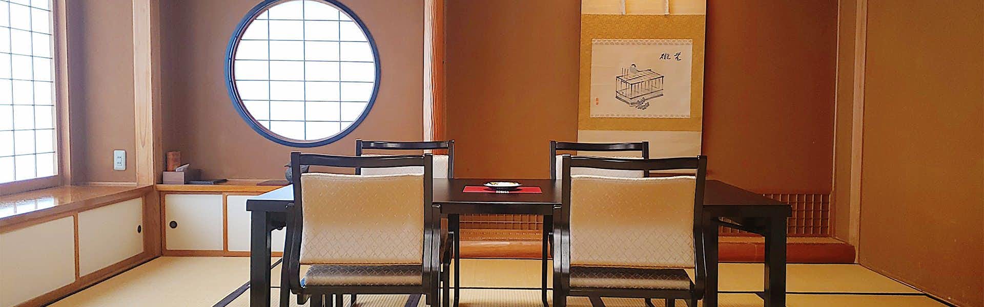 Zenkoji Fuchinobo Two wooden chairs with beige upholstered seats, round window with blue frame, and interior wall space